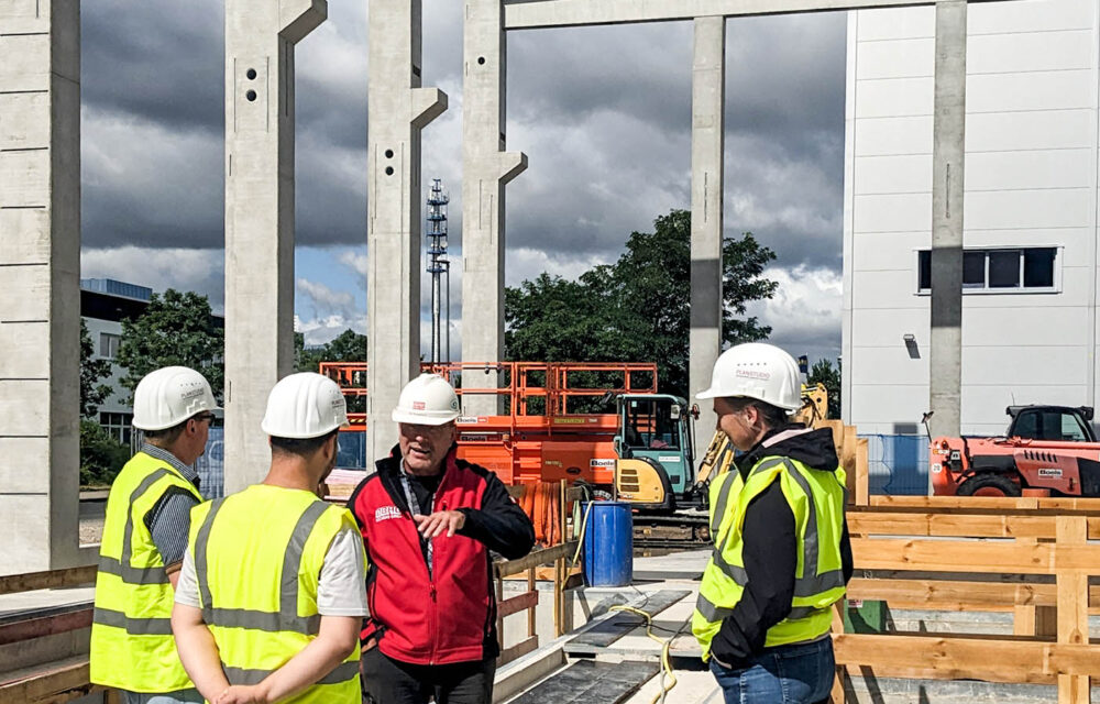 ps360_besuch_siemens_energy_beitragsbild Gruppe von Menschen mit Bauhelmen und Warnwesten auf der Baustelle. Eine Person erklärt zusammenhänge auf der Baustelle.